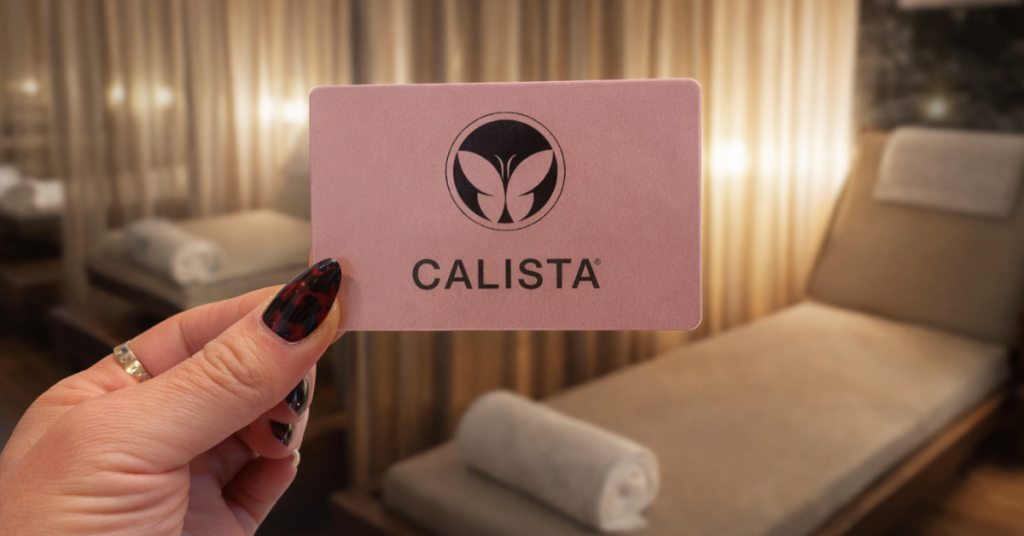 Hand holding a spa gift card in a relaxing spa treatment room setting.